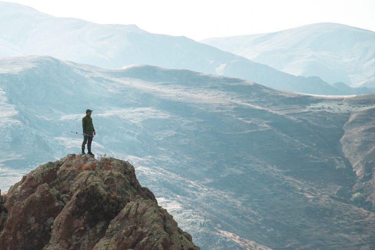 Banner para texto sobre scale-ups e hacks de crescimento: homem visto de costas no topo de uma montanha, olhando um horizonte com várias outras montanhas.